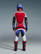 Alpinestars 2026 Techstar Knif Jersey, maglia da motocross, nero, bianco e rosso, vista posteriore su un pilota con pantaloni e attrezzatura coordinati, vivace pannello posteriore rosso, pantaloni bianchi con sfumature blu e loghi rossi, kit da gara professionale per fuoristrada