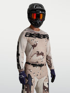 Alpinestars Maglia Racer Lone, maglia da motocross da uomo, colore sabbia desert camo e nero, tessuto tecnico traspirante, vestibilità race, indossata con casco e occhiali per sessioni off-road.