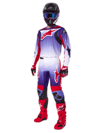 Pilota di motocross con completo Alpinestars 2025 Fluid Wurx, maglia viola e rosso acceso con accenti bianchi, pantaloni da motocross coordinati, stivali rosso acceso, casco nero con maschera blu e guanti rossi e neri, kit professionale completo per fuoristrada