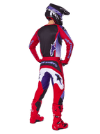Pilota di motocross visto da dietro che indossa il completo Alpinestars 2025 Fluid Wurx, maglia Purple Bright Red con pannello posteriore nero, pantaloni da motocross coordinati con accenti bianchi e viola, stivali rosso brillante e casco nero, abbigliamento professionale da gara fuoristrada