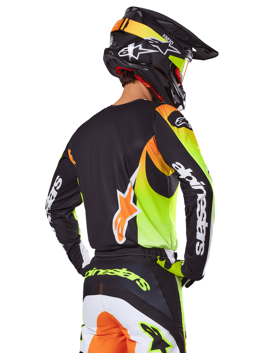 Pilota di motocross visto da dietro con set Alpinestars 2025 Fluid Wurx, maglia nera con grafiche giallo neon e arancione, pantaloni coordinati con pannelli bianchi e arancioni, casco nero con accenti neon, branding Alpinestars su maniche e seduta