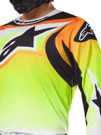 Maglia Alpinestars Fluid Wurx 2025, maglia da motocross, giallo fluorescente con grafiche nere e arancioni, con un grande logo Alpinestars nero sul petto e sulla spalla, indossata da un pilota con casco nero