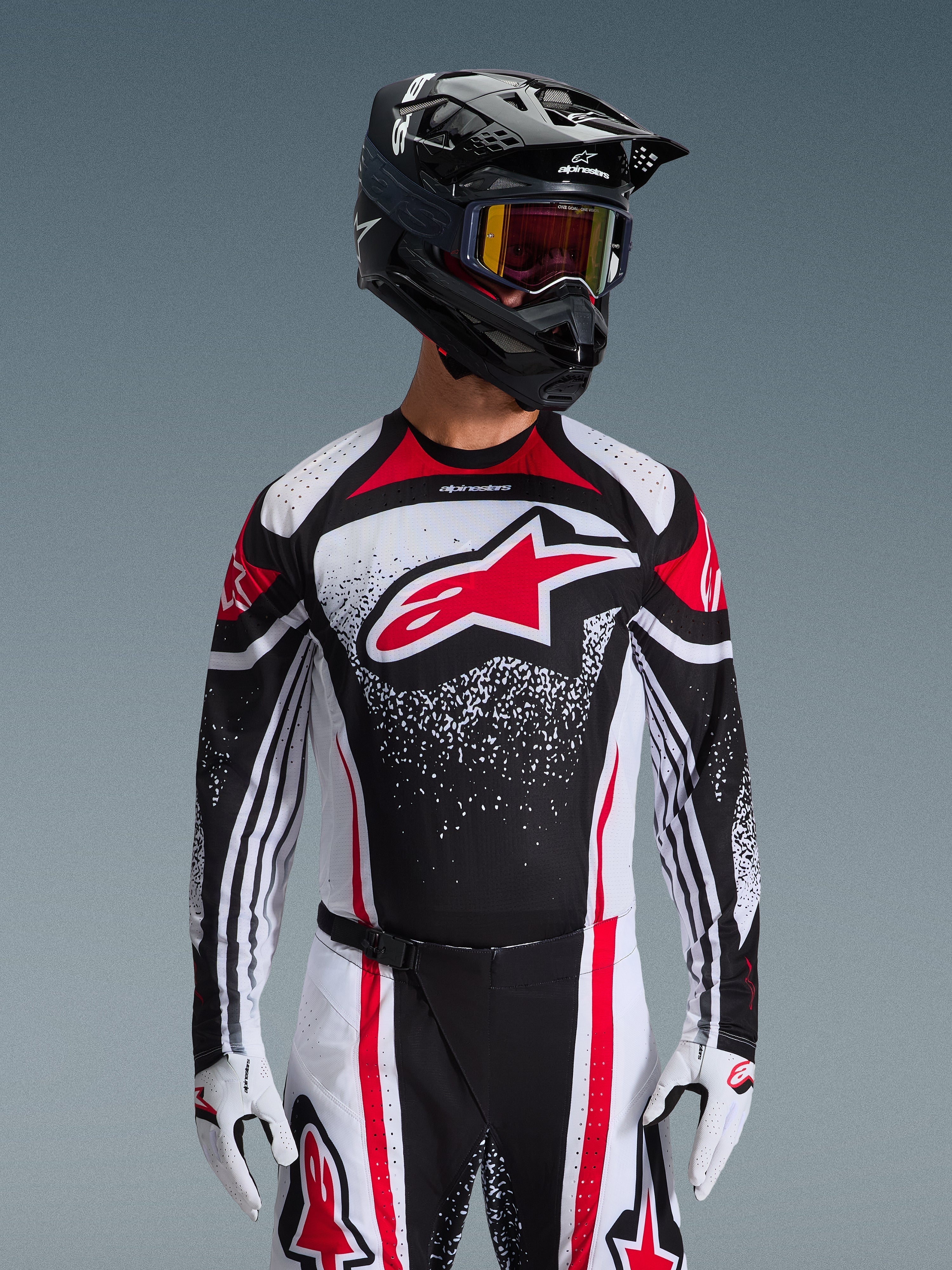 Alpinestars Maglia Techstar Nomur 2026, maglia da motocross, nero, bianco e rosso, indossata da un pilota con pantaloni coordinati, casco nero e guanti bianchi, con un grande logo Astars rosso e grafica punteggiata, vestibilità atletica da gara per competizioni off-road