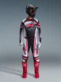 Pilota di motocross con Set Completo Alpinestars 2026 Techstar Nomur, nero, bianco e rosso, maglia con grande logo stella rosso e motivo punteggiato, pantaloni coordinati con pannelli laterali rossi, casco nero con maschera oscurata e stivali rossi.