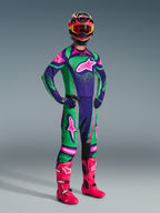 Pilota di motocross che indossa il set completo Alpinestars 2026 Techstar Nomur in viola scuro, verde e rosa fluo, composto da maglia e pantaloni coordinati, casco colorato con maschera rosa e vivaci stivali rosa, equipaggiamento professionale per corse fuoristrada.