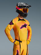 Pilota di motocross che indossa la maglia Alpinestars 2026 Techstar Nomur in arancione, giallo e rosa, con un grande logo a stella nero, casco, maschera e guanti coordinati, abbigliamento professionale da gara per competizioni off-road.
