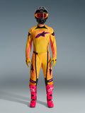 Set completo motocross 2026 Techstar Nomur, abbigliamento da gara completo indossato da un pilota, maglia con sfumatura giallo e arancione e logo stella rosa, pantaloni e guanti coordinati, stivali rosa acceso e casco nero, kit MX professionale su sfondo grigio