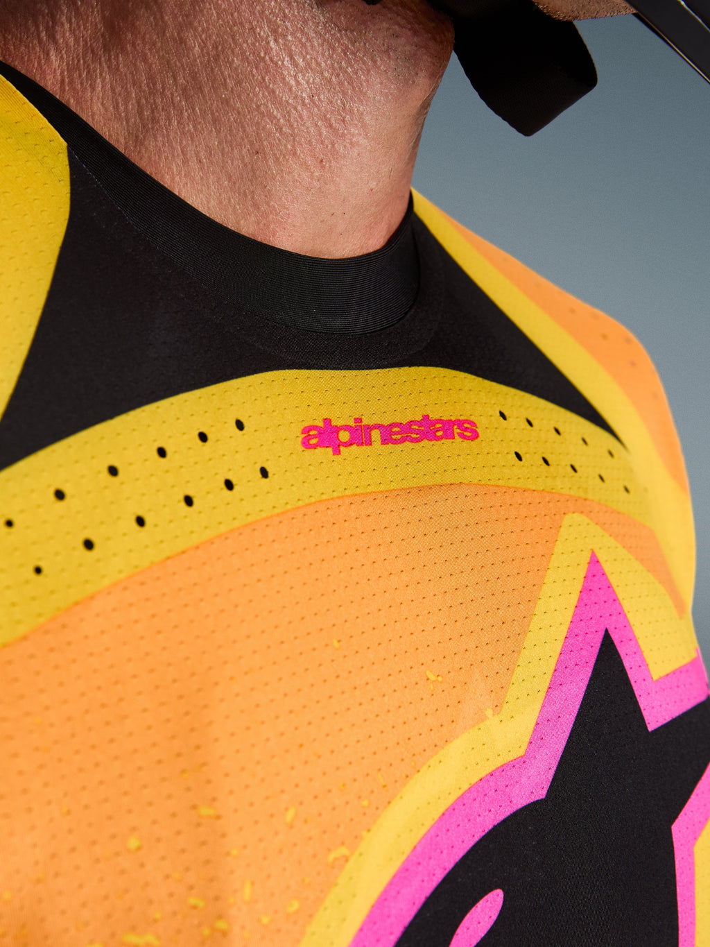 Alpinestars 2026 Techstar Nomur Jersey, maglia da motocross, arancione giallo rosa, dettaglio ravvicinato del petto e del colletto, con ventilazione tagliata al laser, marchio rosa e tessuto mesh traspirante