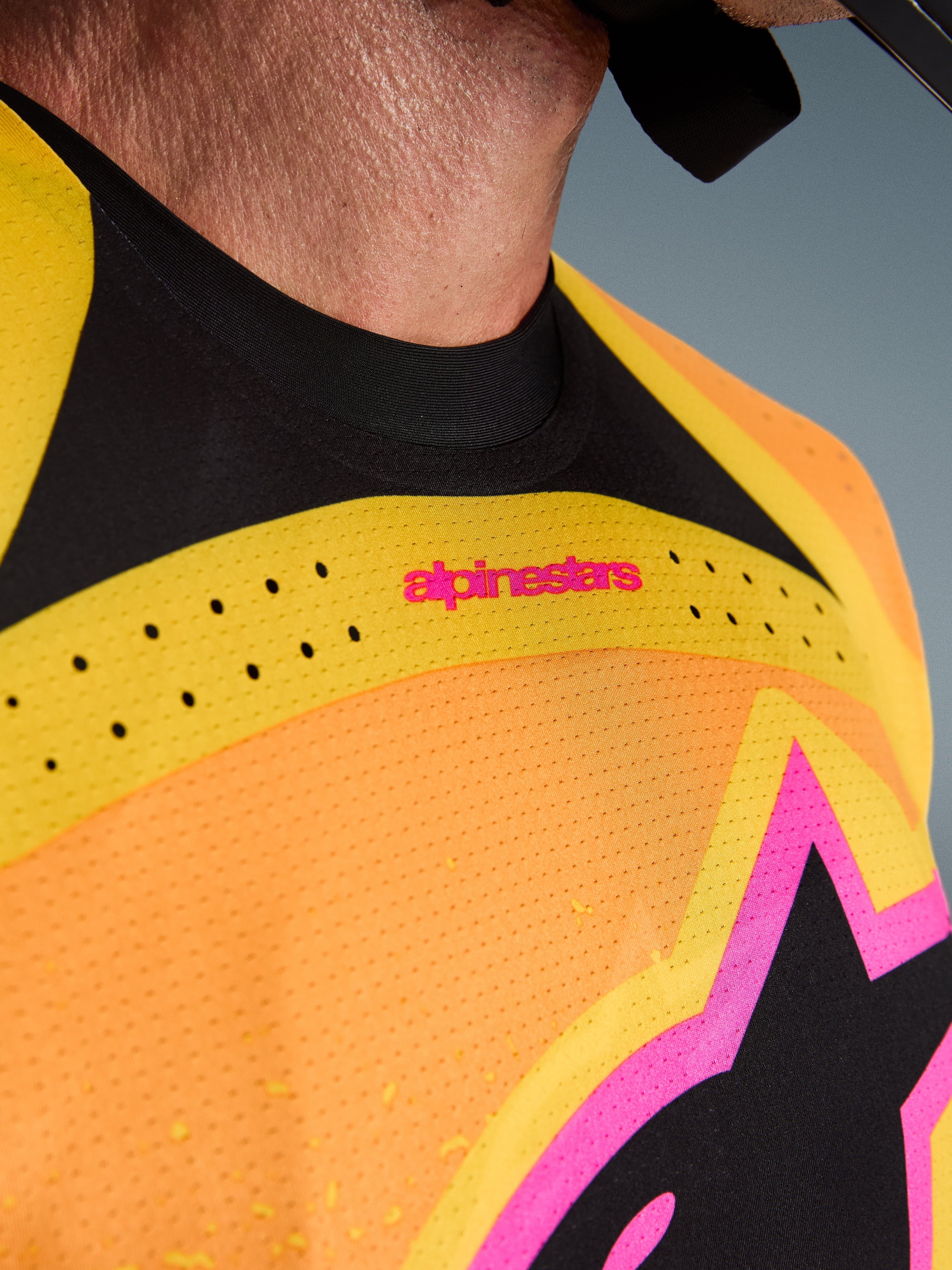 Alpinestars 2026 Techstar Nomur Jersey, maglia da motocross, arancione giallo rosa, dettaglio ravvicinato del petto e del colletto, con ventilazione tagliata al laser, marchio rosa e tessuto mesh traspirante