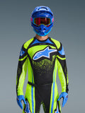 Pilota di motocross che indossa la maglia Alpinestars Techstar Nomur 2026 in blu scuro e giallo fluo con accenti blu, caratterizzata da un grande logo blu sul petto, casco e occhiali blu coordinati, abbigliamento da gara coordinato per competizioni fuoristrada