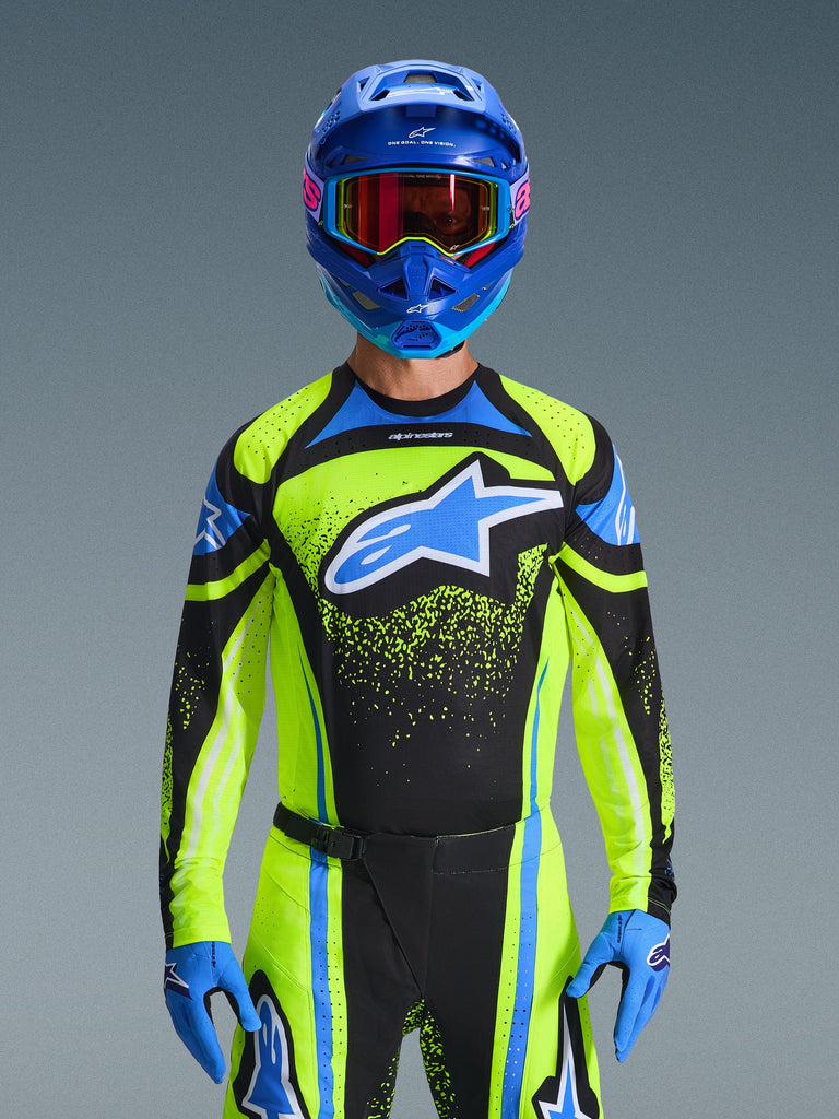 Pilota di motocross che indossa la maglia Alpinestars Techstar Nomur 2026 in blu scuro e giallo fluo con accenti blu, caratterizzata da un grande logo blu sul petto, casco e occhiali blu coordinati, abbigliamento da gara coordinato per competizioni fuoristrada