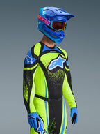 Pilota di motocross con completo Alpinestars 2026 Techstar Nomur, maglia giallo neon e blu con pannelli neri, grande logo blu e bianco sul petto, casco blu coordinato con occhiali arancioni, guanti blu e neri, equipaggiamento ad alte prestazioni per fuoristrada