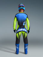 Vista posteriore di un pilota con il completo Alpinestars 2026 Techstar Nomur, maglia blu e giallo neon con accenti neri a effetto spray, pantaloni coordinati con grande logo 'astars' blu sulla seduta, stivali blu con loghi bianchi e casco blu e nero, abbigliamento professionale da motocross