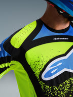 Maglia Alpinestars Techstar Nomur 2026, primo piano del petto e della spalla in Dark Navy, Giallo Fluo e Blu, con perforazioni per la ventilazione tagliate al laser, colletto incollato senza cuciture e logo Alpinestars in evidenza, abbigliamento tecnico da motocross.