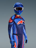 Alpinestars 2026 Techstar Nomur Gear Set, maglia e pantaloni da motocross in blu scuro, arancione e blu UCLA, indossato da un pilota con casco e guanti blu coordinati, con grafiche del logo audaci e vestibilità atletica race fit.