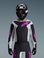 Alpinestars Set Completo Fluid Grid 2026, pilota di motocross che indossa una maglia nera, bianca e rosa con pantaloni coordinati, casco nero con accenti rosa e bianchi, abbigliamento professionale coordinato per prestazioni fuoristrada