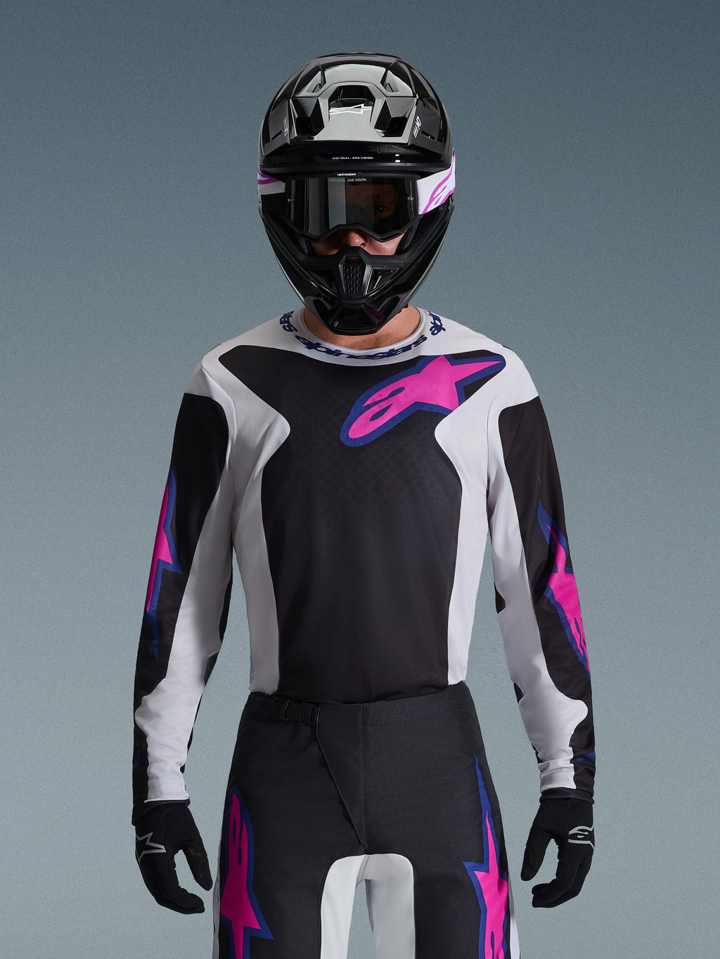 Alpinestars 2026 Fluid Grid Jersey, maglia da motocross, nero, grigio chiaro e viola, indossata da un pilota con pantaloni off-road coordinati, casco nero e occhiali, set completo di abbigliamento tecnico da gara