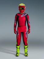 Pilota di motocross con Maglia Fluid Grid 2026 in rosso, nero e viola, pantaloni rossi coordinati con loghi viola, casco rosso con accenti giallo neon e stivali giallo neon, kit da gara completo per motocross off-road