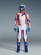 Pilota di motocross con equipaggiamento da gara completo, maglia Fluid Grid 2026 in arancione e blu UCLA, pantaloni bianchi coordinati con accenti arancioni e blu, casco blu e bianco con maschera blu, stivali da fuoristrada blu e viola, guanti blu, completo coordinato per corse di motocross