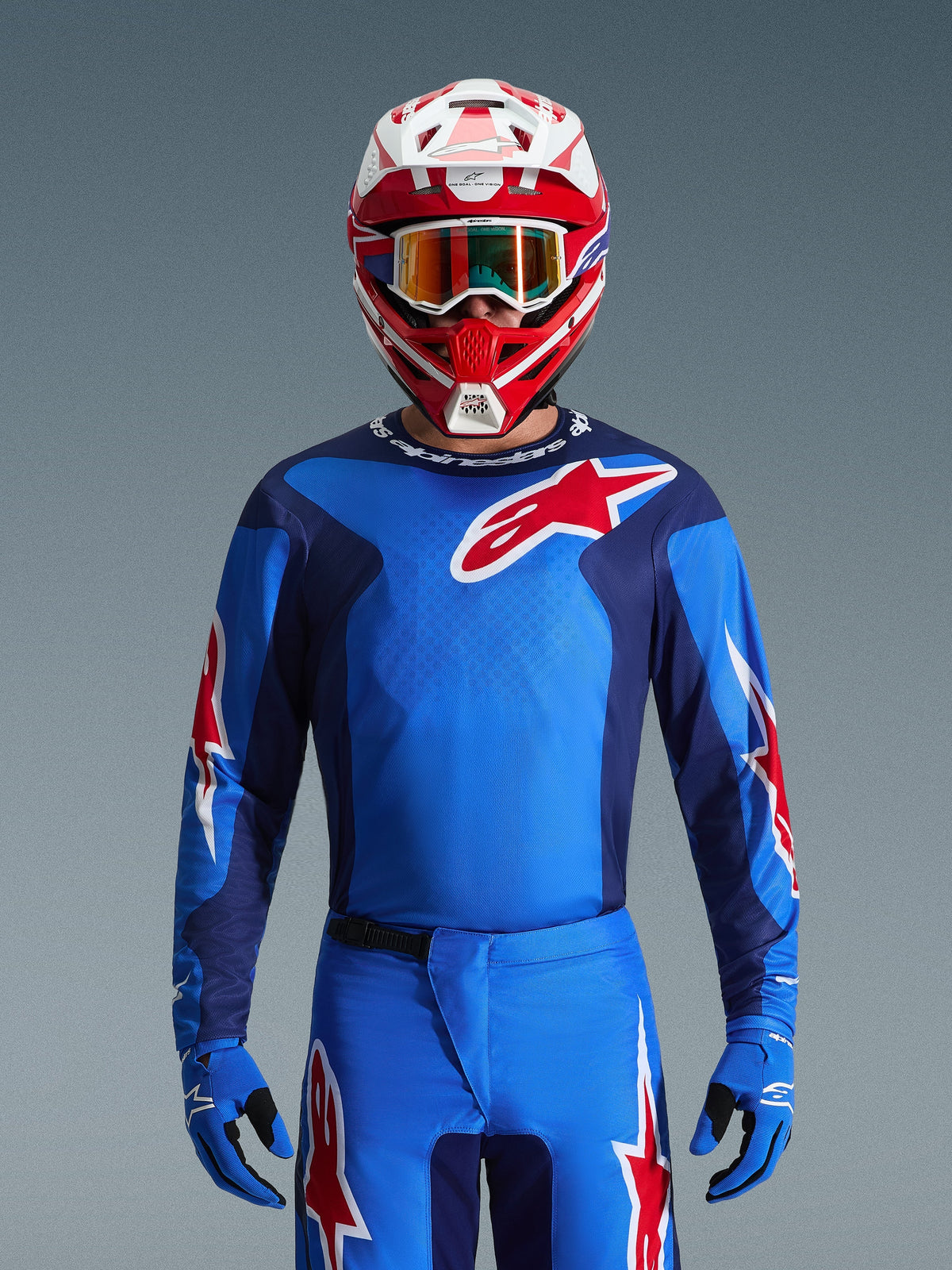 Alpinestars 2026 Fluid Grid Jersey, maglia da motocross blu e rossa, indossata con pantaloni coordinati e casco rosso e bianco, con evidenti loghi a stella rossi e vestibilità atletica per prestazioni fuoristrada