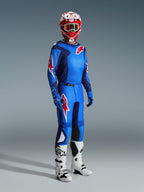 Pilota di motocross che indossa la maglia Alpinestars 2026 Fluid Grid in Blue Red, abbinata a pantaloni da motocross coordinati, stivali bianchi e neri e un casco rosso e bianco, set di abbigliamento professionale per prestazioni off-road.