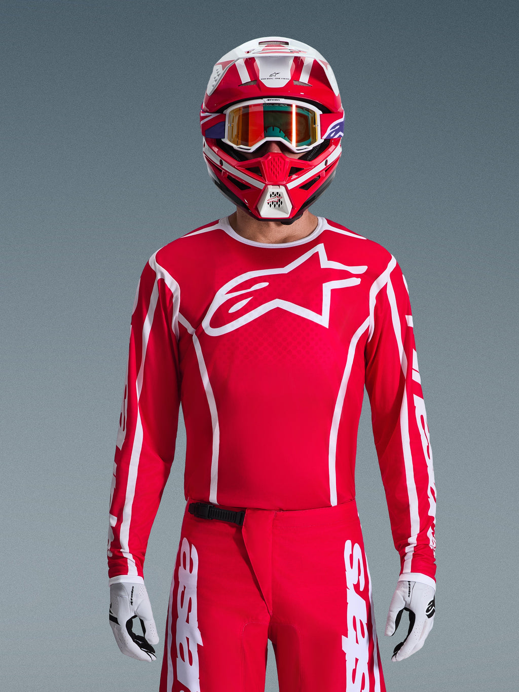 Pilota di motocross con completo Alpinestars 2026 Fluid Apex Gear Set, maglia rossa con grande logo a stella bianco sul petto, pantaloni rossi coordinati con branding bianco, casco rosso e bianco con occhiali iridescenti, guanti bianchi e neri, outfit rosso e bianco coordinato per corse off-road
