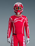 Maglia Alpinestars 2026 Fluid Apex, maglia da motocross, rossa e bianca, indossata da un pilota con casco coordinato rosso e bianco e occhiali arancioni, caratterizzata da un prominente logo bianco sul petto, vestibilità atletica, parte di un set coordinato per corse off-road