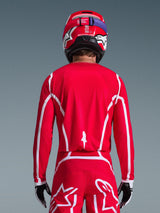 Vista posteriore di un pilota di motocross che indossa la maglia Alpinestars 2026 Fluid Apex in rosso e bianco, con motivi geometrici bianchi, abbinata a pantaloni da motocross coordinati e un casco rosso, abbigliamento completo da gara per prestazioni fuoristrada.