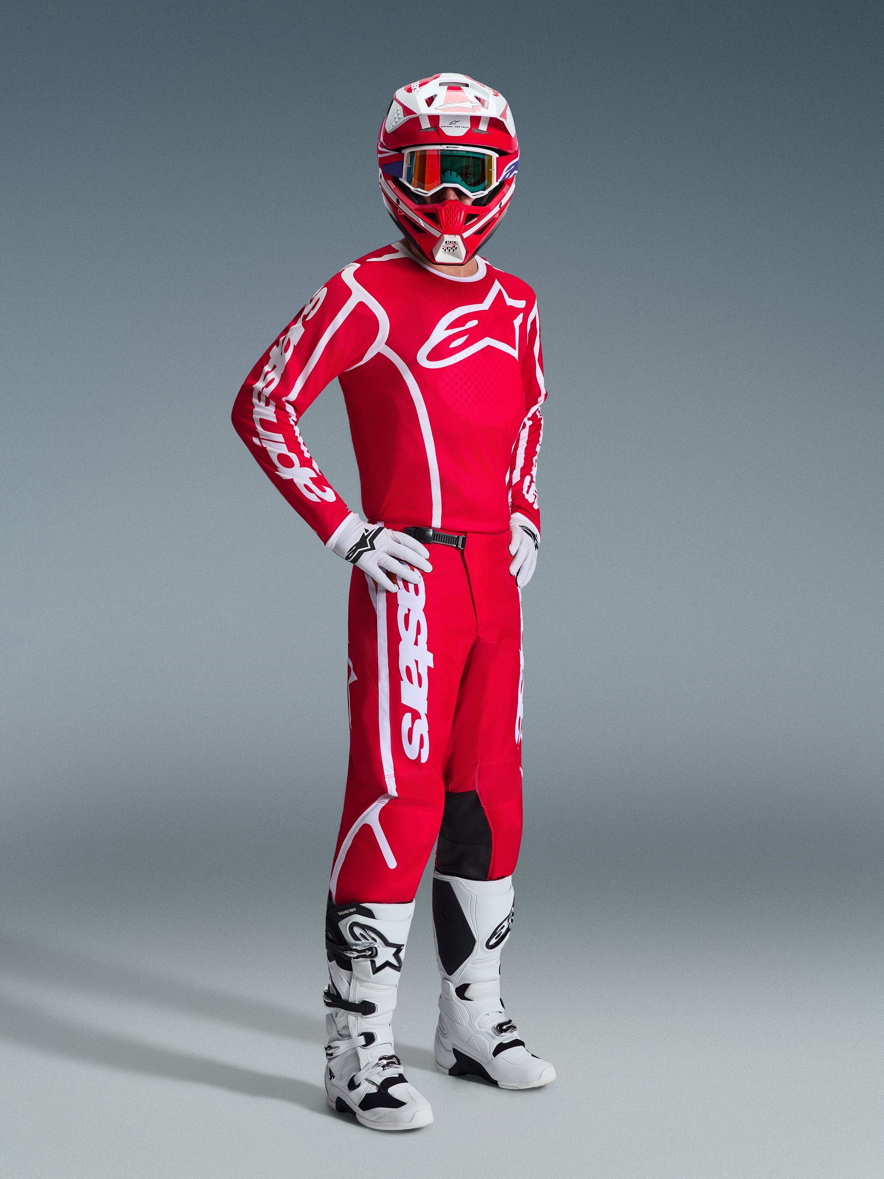 Pilota di motocross con completo Alpinestars 2026 Fluid Apex, maglia rossa con grandi loghi bianchi, pantaloni rossi coordinati con branding bianco, casco bianco e rosso, stivali e guanti da motocross bianchi, outfit coordinato per gare off-road