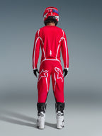 Vista posteriore di un pilota di motocross con il completo Alpinestars 2026 Fluid Apex, maglia e pantaloni rosso acceso con strisce e loghi bianchi, abbinati a stivali bianchi e neri e casco rosso, kit da corsa professionale per fuoristrada