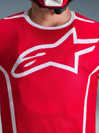 Primo piano della maglia Alpinestars Fluid Apex 2026 in rosso e bianco, caratterizzata da un grande logo Astars bianco sul petto, costruzione in mesh poly-fabric traspirante e bordo del colletto bianco, abbigliamento da motocross