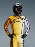Alpinestars 2026 Fluid Apex Jersey, maglia da motocross, giallo e nero con una manica bianca e un grande logo nero sul petto, indossata come parte di un set completo da gara con pantaloni coordinati, casco nero e guanti