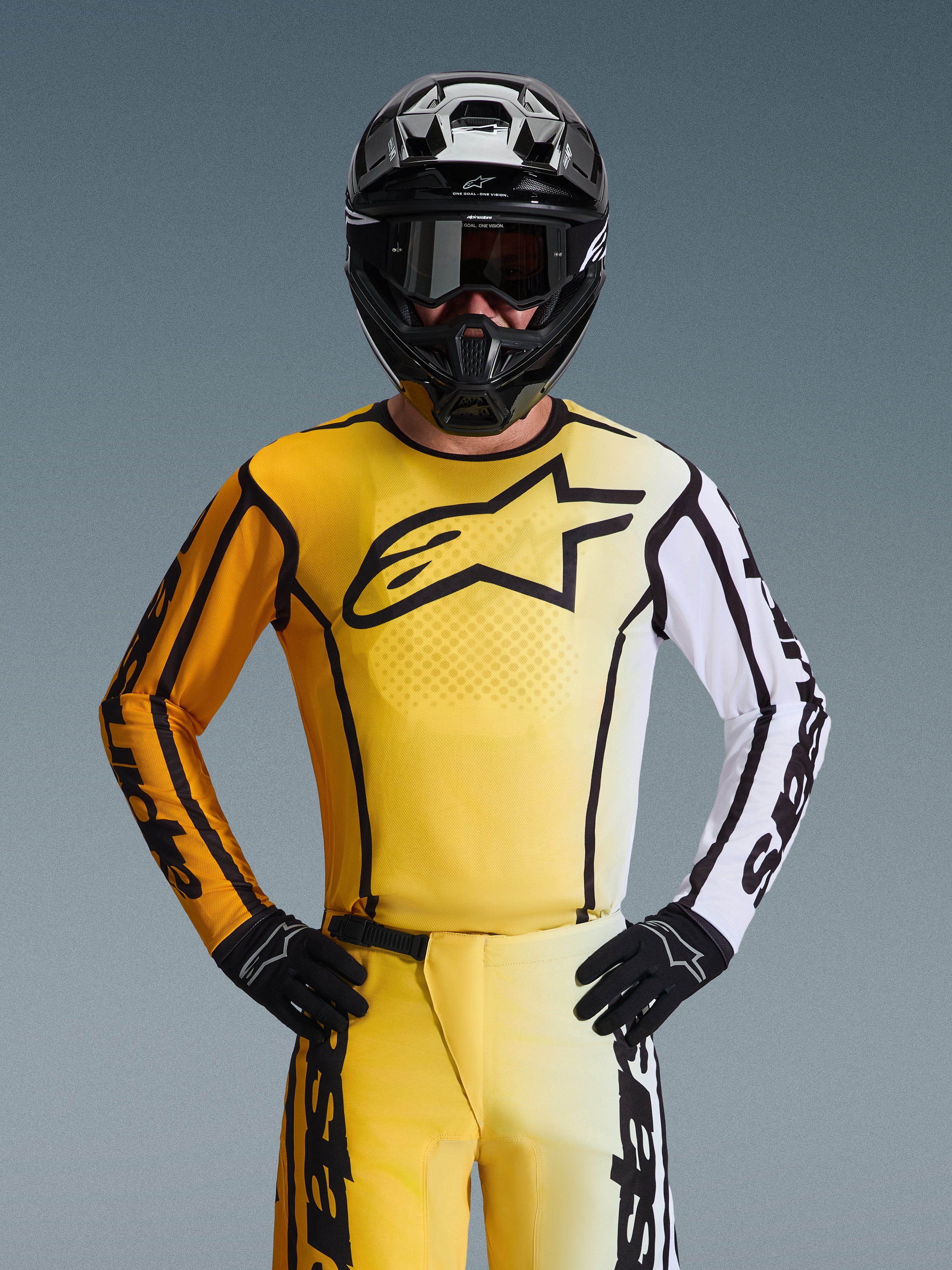 Alpinestars 2026 Fluid Apex Jersey, maglia da motocross, giallo e nero con una manica bianca e un grande logo nero sul petto, indossata come parte di un set completo da gara con pantaloni coordinati, casco nero e guanti