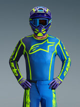Pilota di motocross che indossa la maglia Alpinestars 2026 Fluid Apex in Blue Yellow Fluo, caratterizzata da una base blu vibrante con grafiche giallo fluorescente e un grande logo sul petto, coordinata con casco e guanti abbinati, progettata per il fuoristrada e le gare di motocross