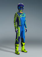 Alpinestars Maglia Fluid Apex 2026, blu e giallo fluo, indossata da un modello in un completo da motocross con pantaloni coordinati, casco viola e giallo e stivali giallo fluo brillanti.