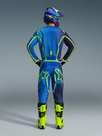 Set completo Alpinestars Fluid Apex 2026, vista posteriore di un pilota di motocross con maglia blu e navy e pantaloni coordinati con vivaci accenti verde neon, stivali giallo neon e casco viola, abbigliamento professionale da corsa fuoristrada