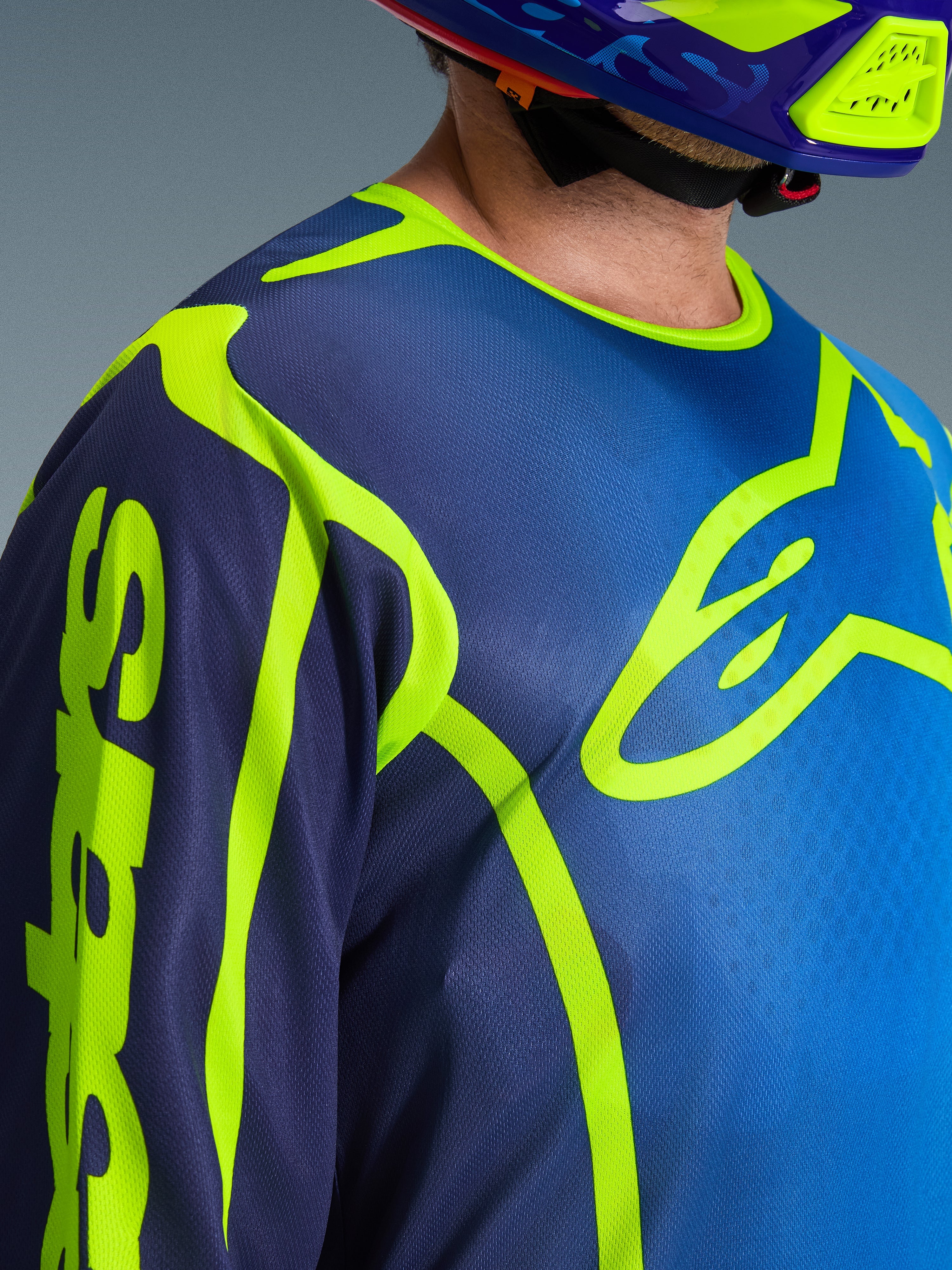 Maglia Alpinestars Fluid Apex 2026, maglia da motocross in blu e giallo fluo, vista ravvicinata del logo giallo neon sul petto e branding sulla manica, struttura in poliestere traspirante con colletto sportivo ergonomico