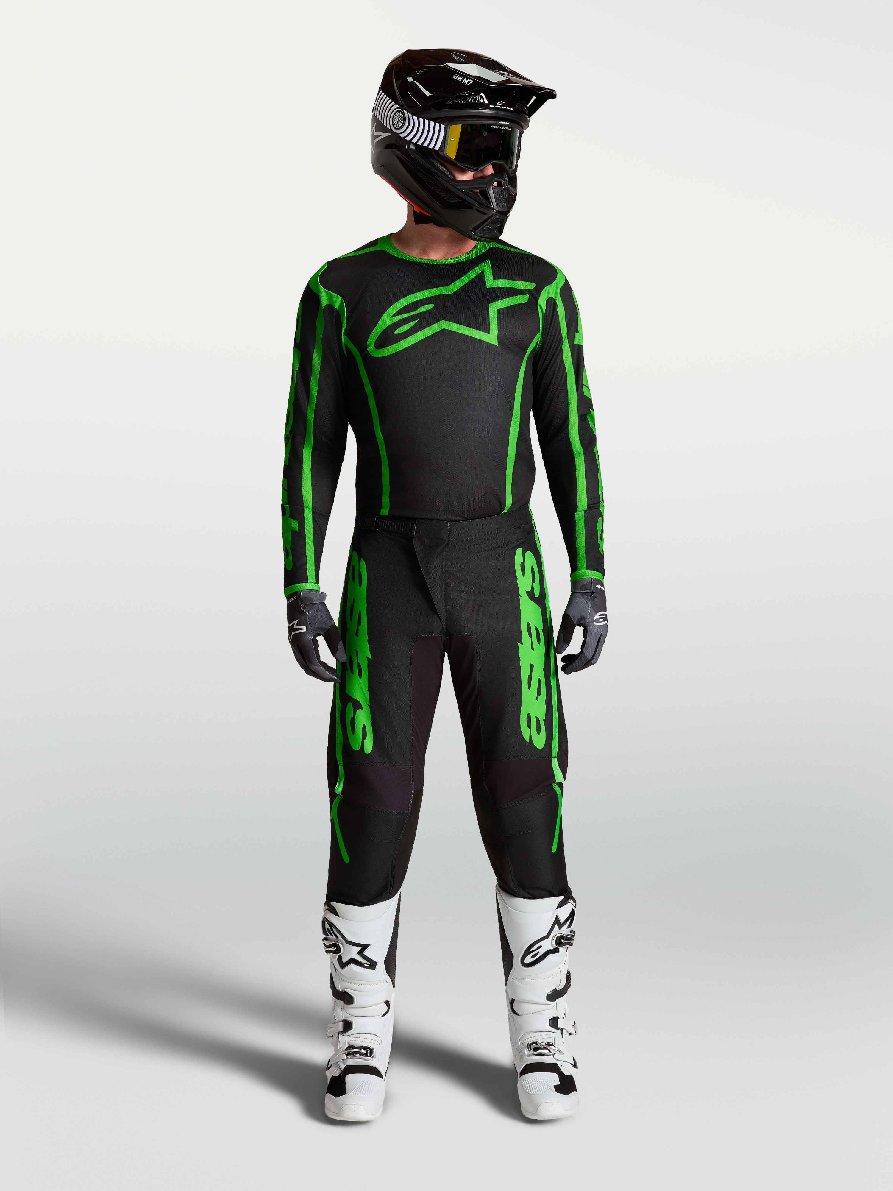 Alpinestars Maglia Fluid Apex V2 e Fluid Apex V2 Gear Set, completo motocross da uomo, nero e verde fluo, con pantaloni coordinati e stivali bianchi, abbigliamento tecnico da fuoristrada.