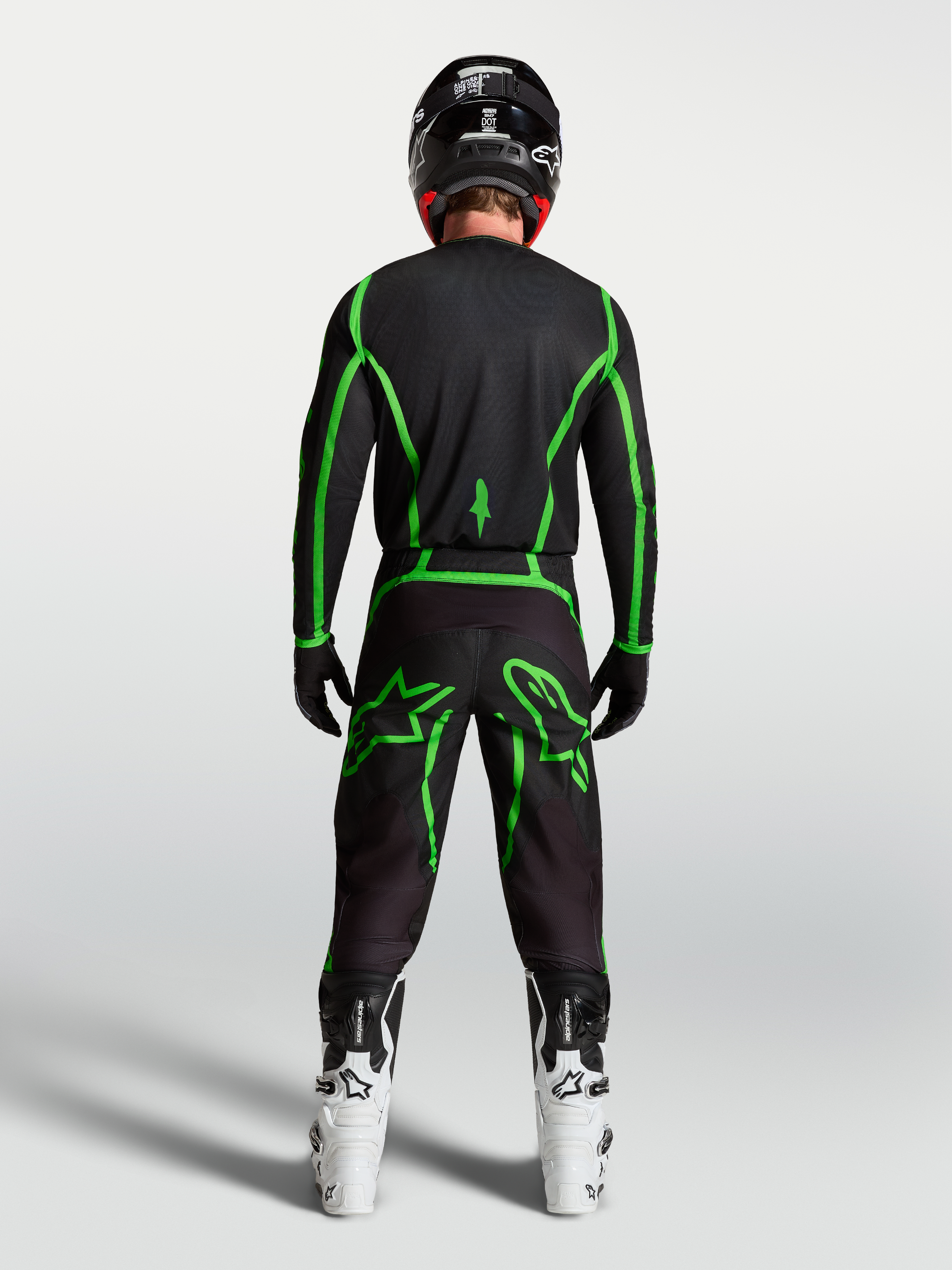 Alpinestars Pantaloni Fluid Apex V2, pantaloni da motocross da uomo, neri e verdi fluo, vista posteriore di un pilota con stivali bianchi.