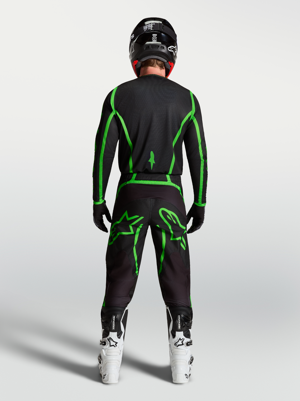 Alpinestars Maglia Fluid Apex V2, maglia da motocross nera e verde fluo, vista posteriore su pilota con stivali bianchi, abbigliamento performance per fuoristrada.