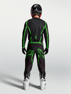 Alpinestars Maglia Fluid Apex V2, maglia da motocross nera e verde fluo, vista posteriore su pilota con stivali bianchi, abbigliamento performance per fuoristrada.
