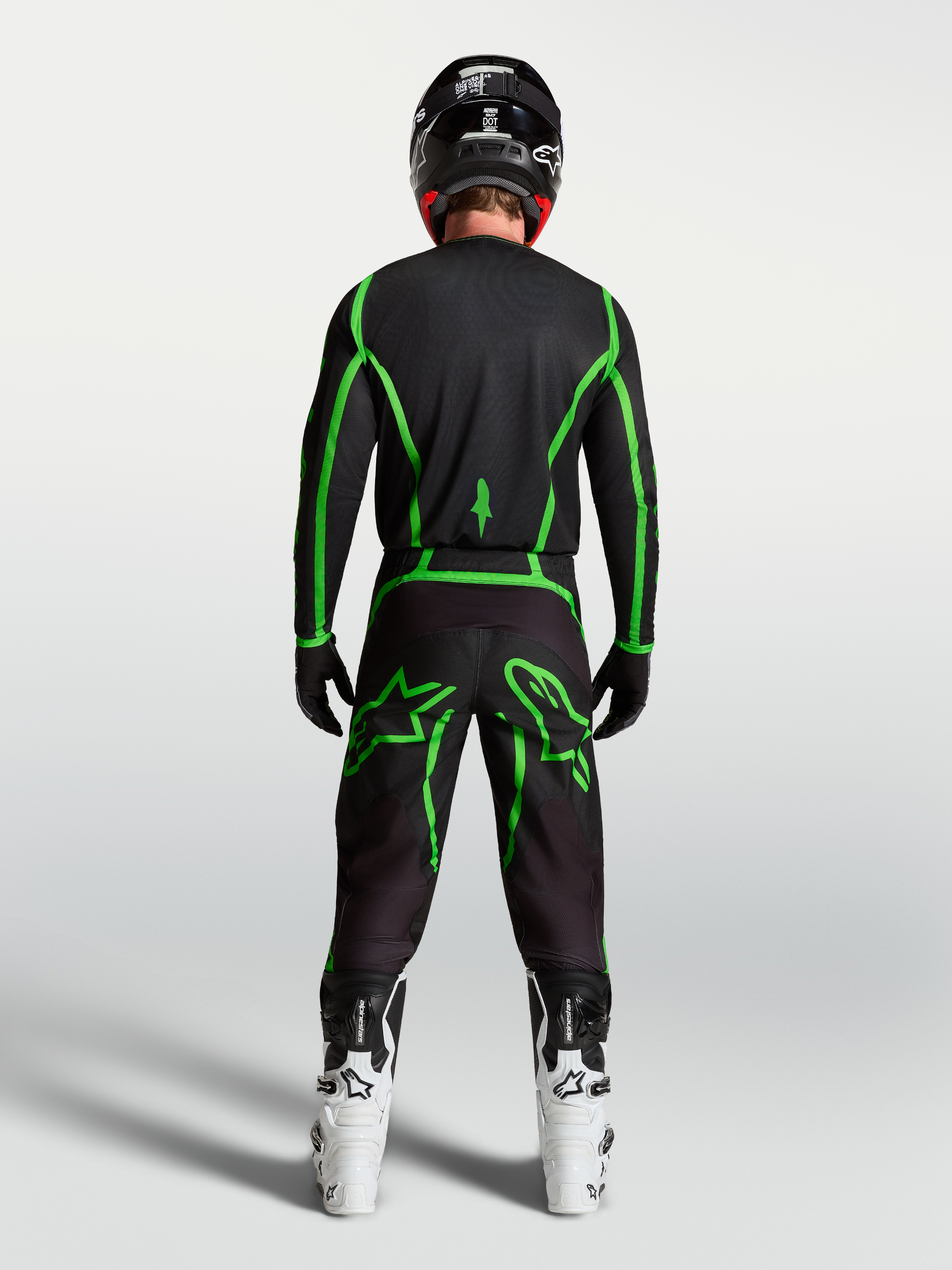 Alpinestars Maglia Fluid Apex V2, maglia da motocross nera e verde fluo, vista posteriore su pilota con stivali bianchi, abbigliamento performance per fuoristrada.