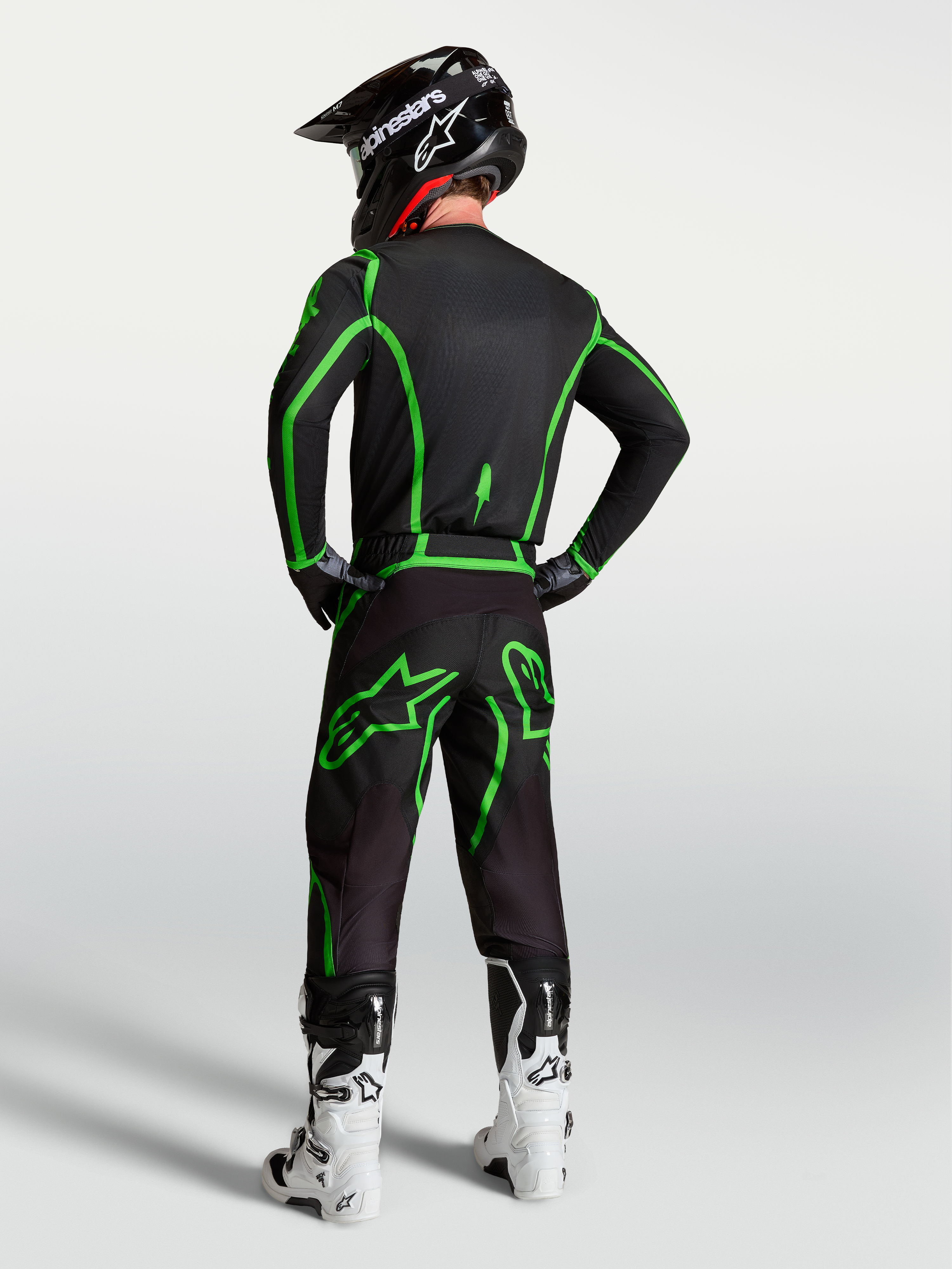 Alpinestars Maglia Fluid Apex V2, maglia da motocross da uomo, nera e verde, vista posteriore del modello con pantaloni coordinati e casco, abbigliamento tecnico per guida off-road