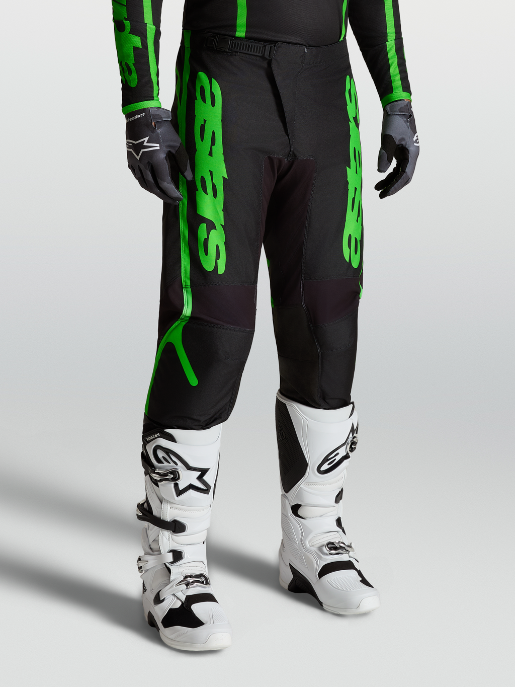 Alpinestars Pantaloni Fluid Apex V2, pantaloni motocross da uomo, nero e verde fluorescente, in tessuto poliestere 600D rinforzato, indossati con stivali bianchi per fuoristrada e MX.