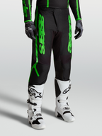Alpinestars Pantaloni Fluid Apex V2, pantaloni motocross da uomo, nero e verde fluorescente, in tessuto poliestere 600D rinforzato, indossati con stivali bianchi per fuoristrada e MX.
