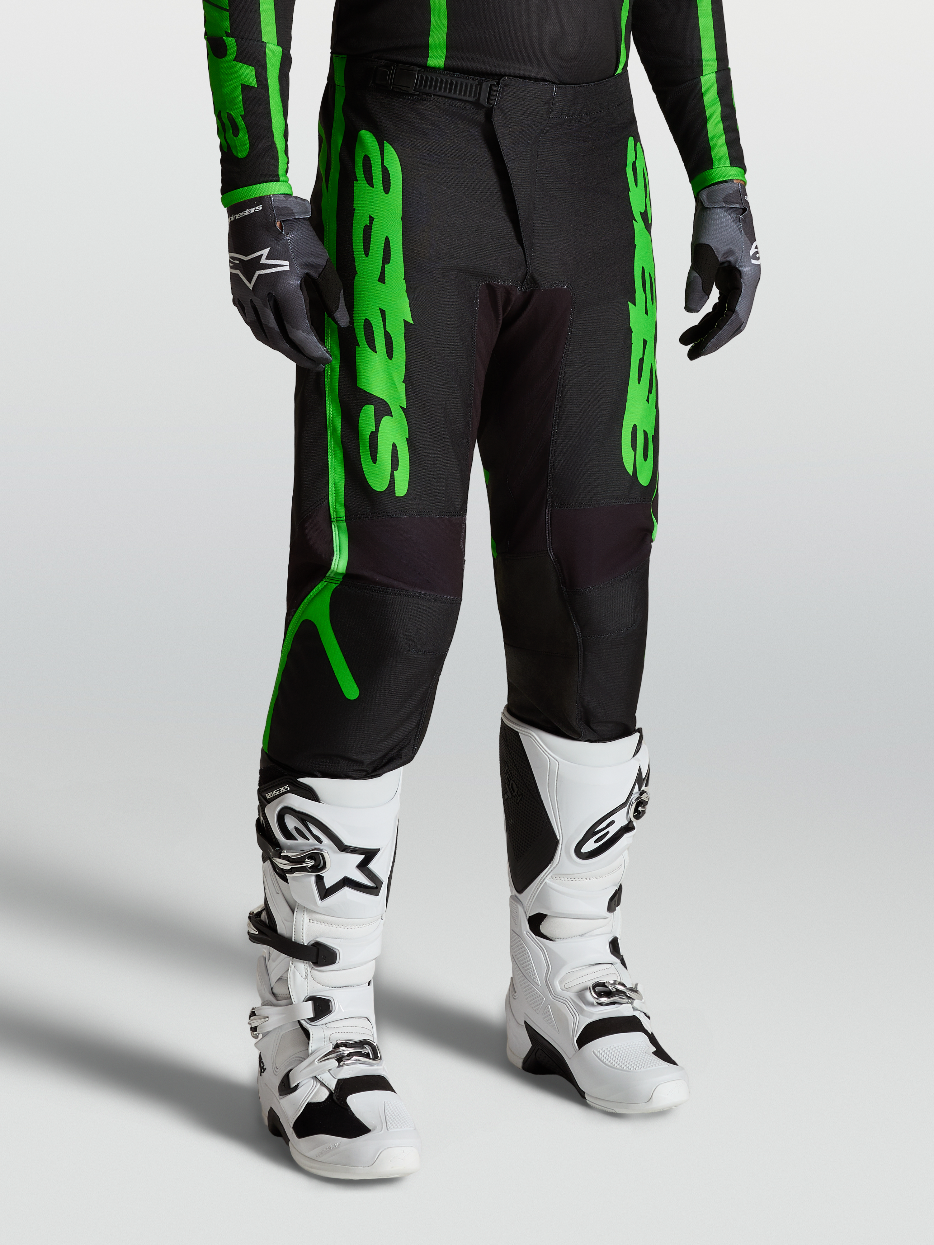 Alpinestars Pantaloni Fluid Apex V2, pantaloni motocross da uomo, nero e verde fluorescente, in tessuto poliestere 600D rinforzato, indossati con stivali bianchi per fuoristrada e MX.