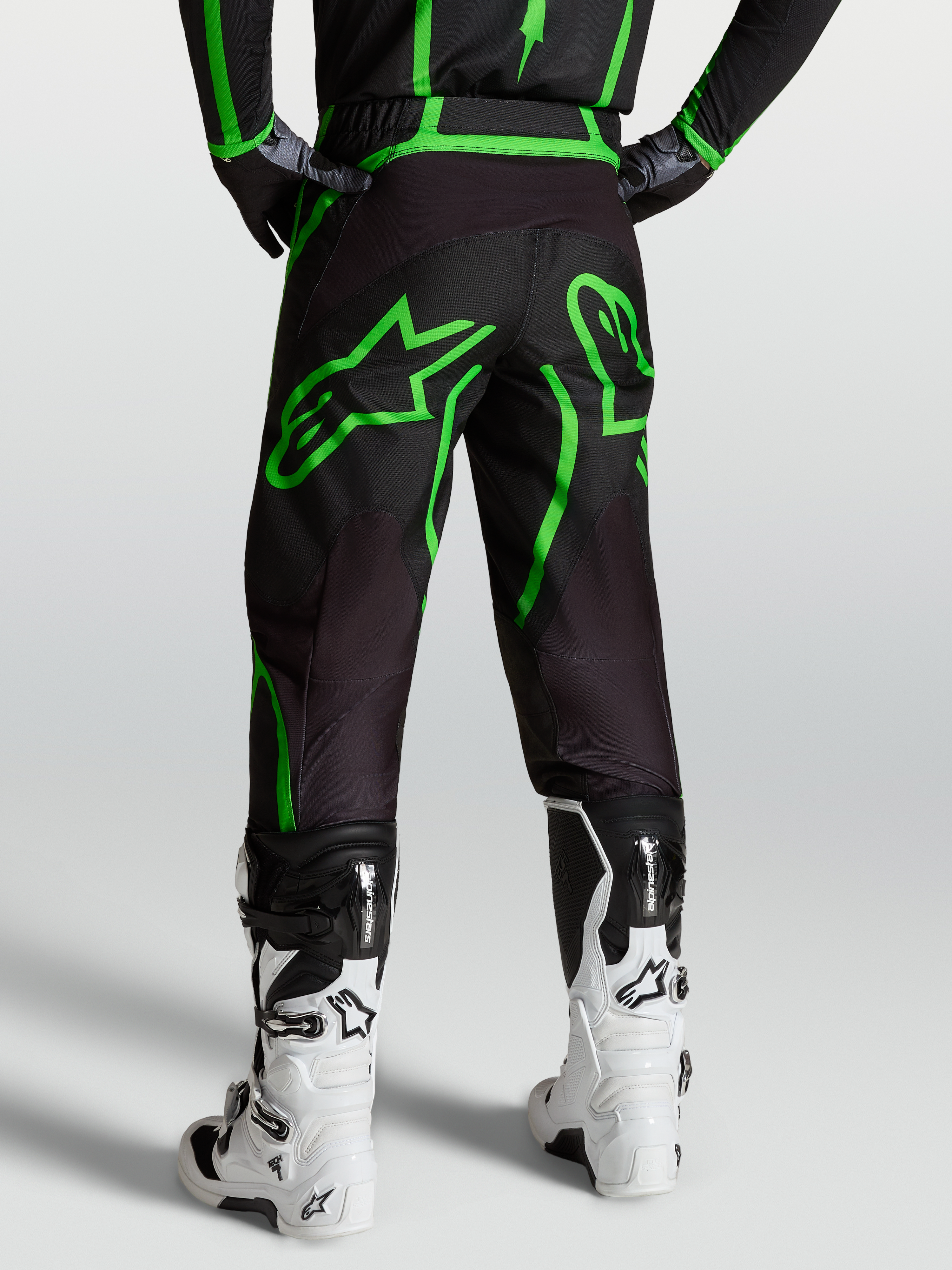 Alpinestars Pantaloni Fluid Apex V2, pantaloni motocross da uomo, nero e verde fluo, vista posteriore su modello con stivali bianchi.