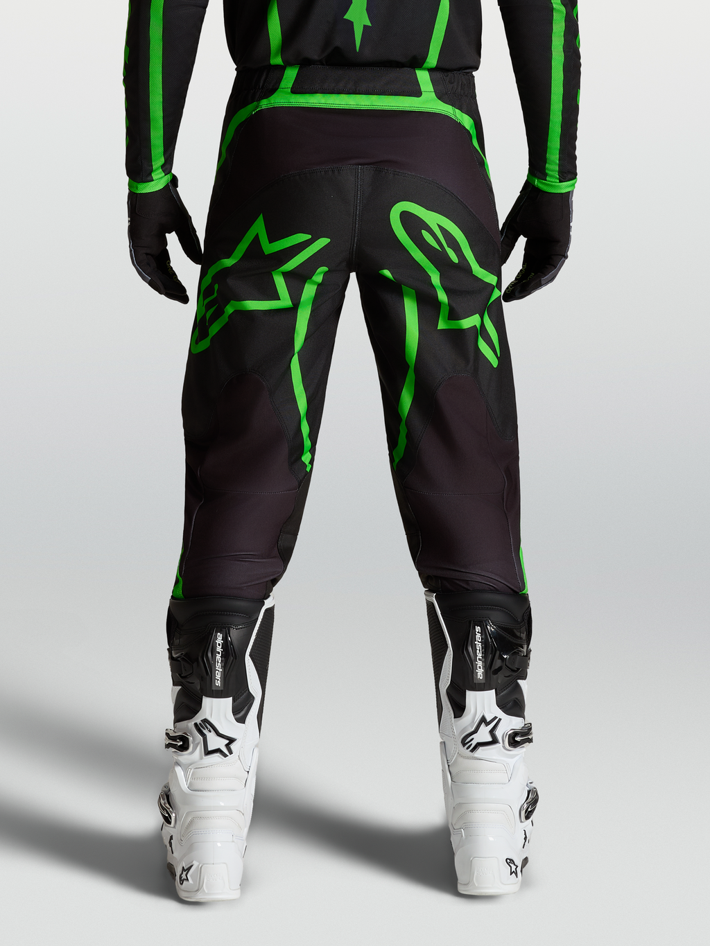 Alpinestars Pantaloni Fluid Apex V2, pantaloni motocross da uomo, nero e verde fluo, vista posteriore su modello con grafiche a stella, abbigliamento fuoristrada tecnico.