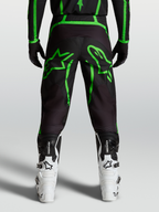 Alpinestars Pantaloni Fluid Apex V2, pantaloni motocross da uomo, nero e verde fluo, vista posteriore su modello con grafiche a stella, abbigliamento fuoristrada tecnico.