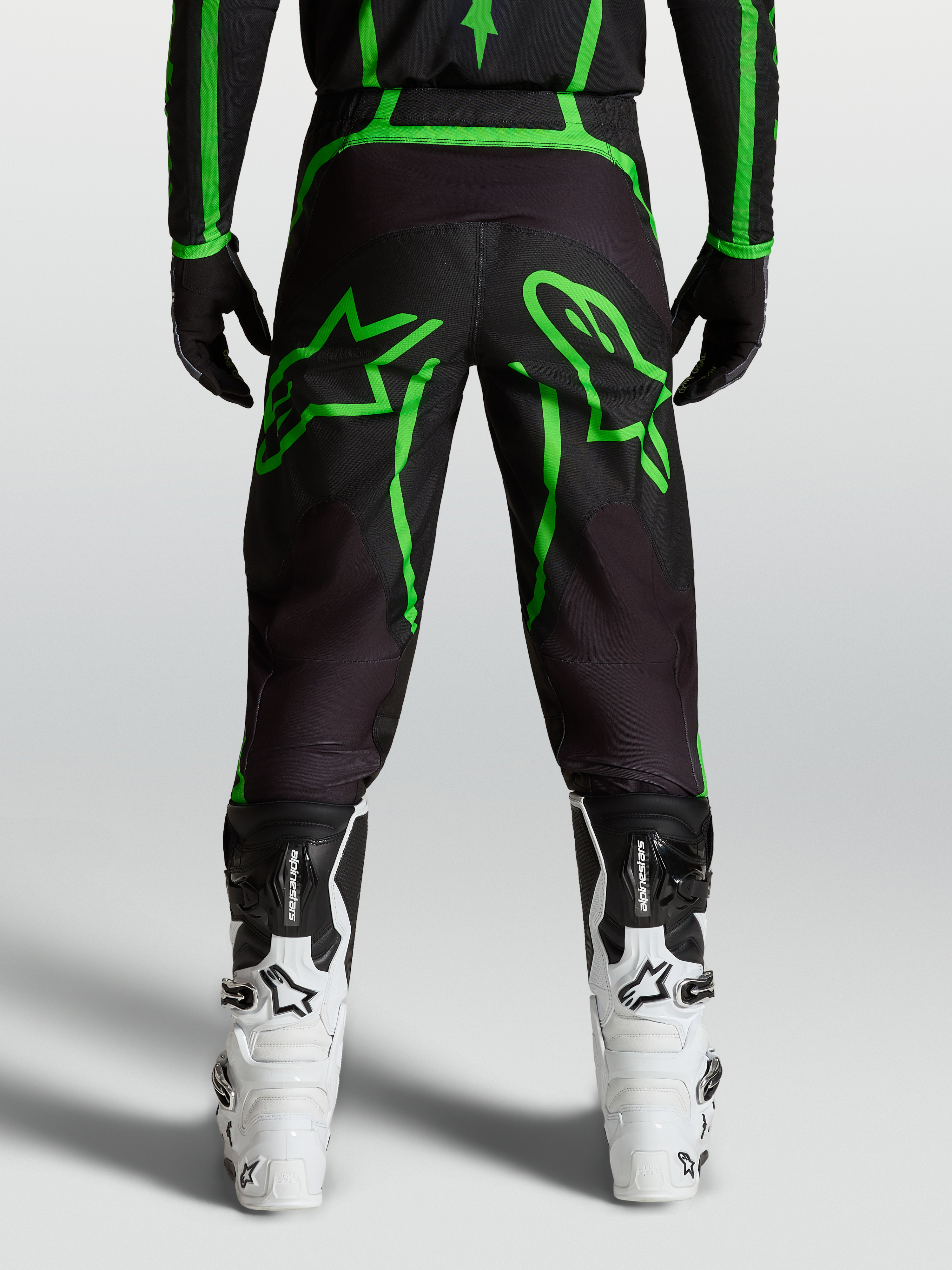 Alpinestars Pantaloni Fluid Apex V2, pantaloni motocross da uomo, nero e verde fluo, vista posteriore su modello con grafiche a stella, abbigliamento fuoristrada tecnico.